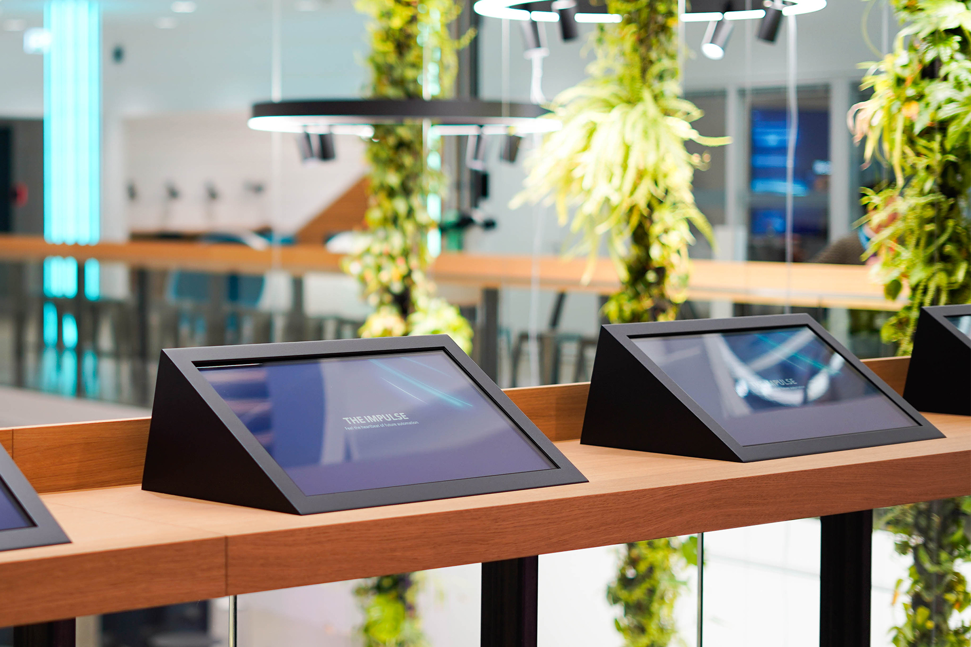 Zwei Touch-Displays zur interaktiven Vertriebspräsentation auf einem Tresen, im Hintergrund herunterhängende Pflanzen