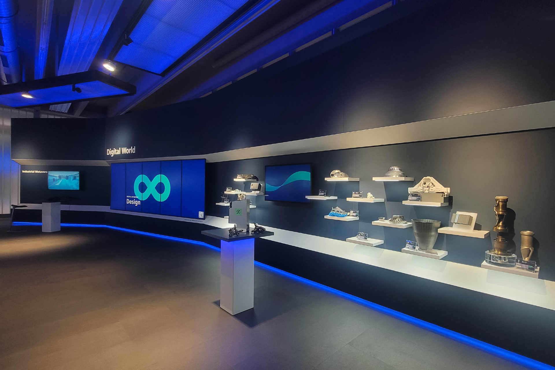 Ausstellungsbereich „Digital World“ mit blauer LED-Wand und digitalen Exponaten an der Wand. Zahlreiche Bauteile und Modelle sind auf kleinen Podesten ausgestellt, begleitet von Touchscreens und Lichtinszenierung in Blau.