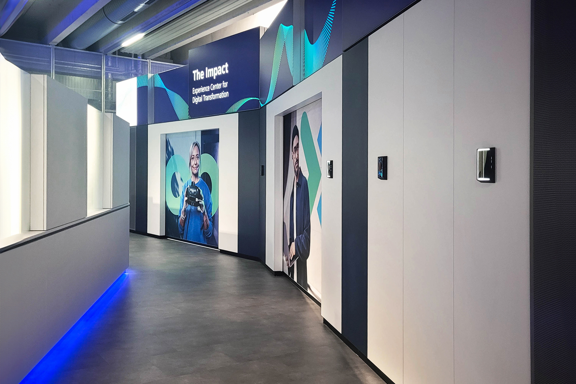 Flurbereich mit großflächigen Porträtbildern und dem Schild „The Impact – Experience Center for Digital Transformation“. Die Wandgestaltung ist modern und einladend, mit indirekter Beleuchtung und klaren Farben.