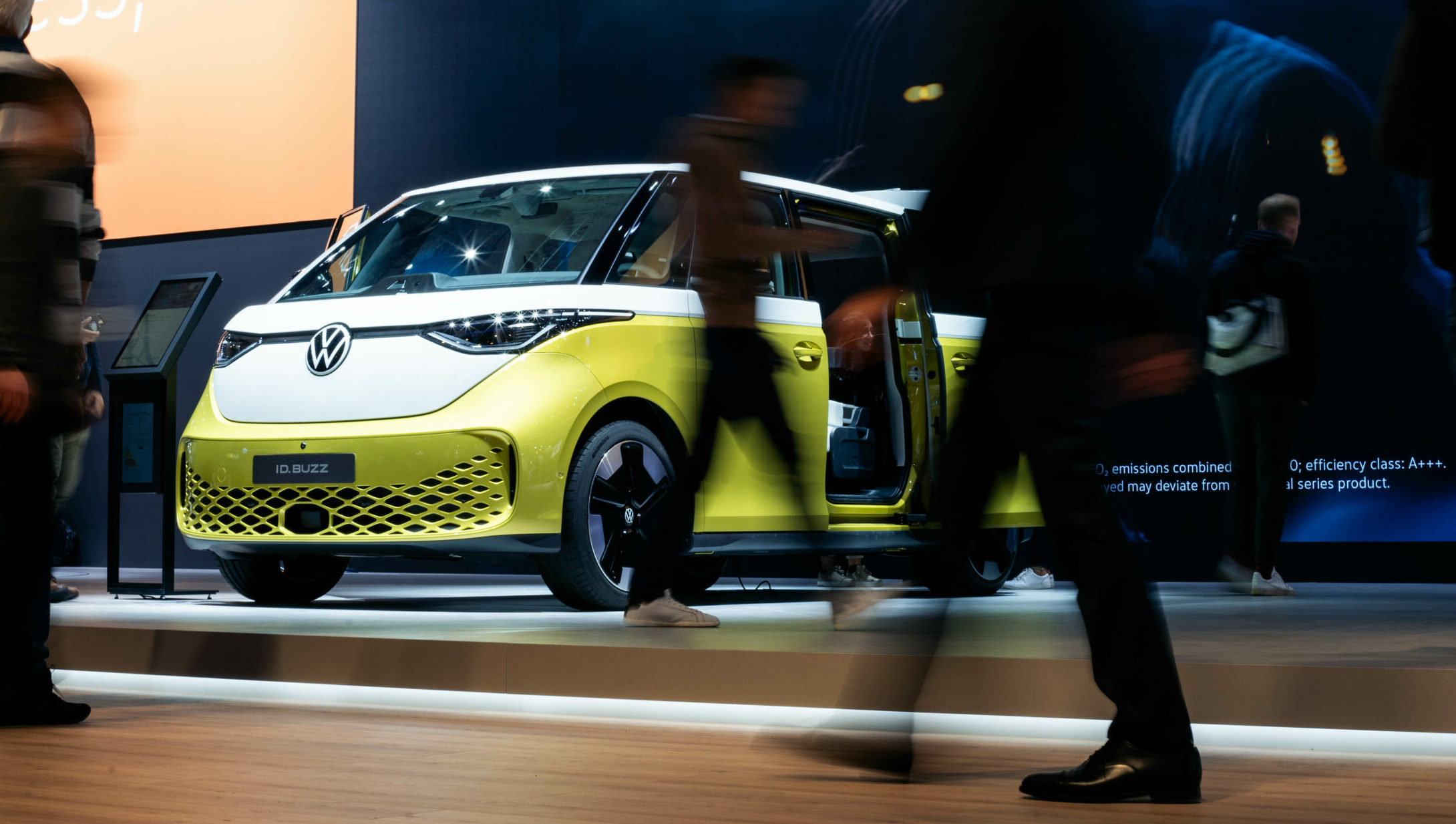Menschen gehen am VW ID. Buzz auf der IAA vorbei – Fahrzeugpräsentation auf Messe mit B12-Touch Lösungen
