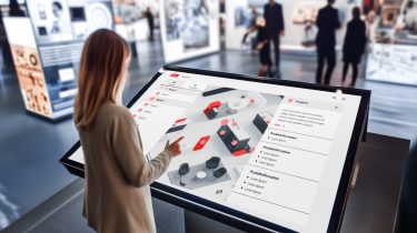 Woman taps on a screen with a digital maps solution from B12-Touch during trade fair - Headless CMS Sales